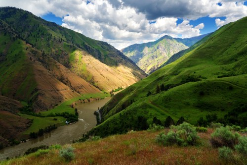Lush green hillsides surround a winding river under a partly cloudy sky, showcasing a serene natural landscape.