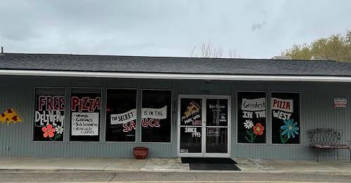 A pizza shop with colorful signs advertising free delivery and special sauce, featuring flowers and a welcoming facade.