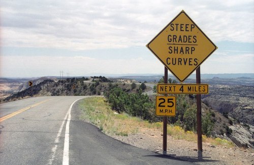 A road sign warns of steep grades and sharp curves for the next four miles, with a speed limit of 25 mph.