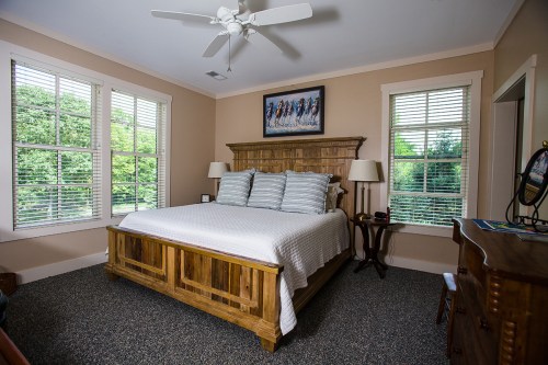 Cozy bedroom with a wooden bed, two lamps, and large windows overlooking greenery.