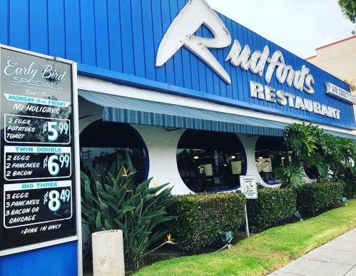 Exterior of Rudfort's Restaurant with a blue facade, menu specials displayed, and greenery in front.