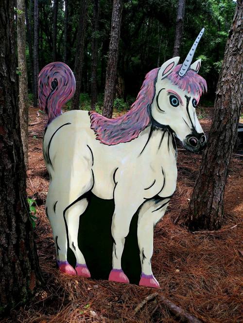 A colorful cutout of a unicorn with a pink mane, set against a backdrop of trees and pine needles.