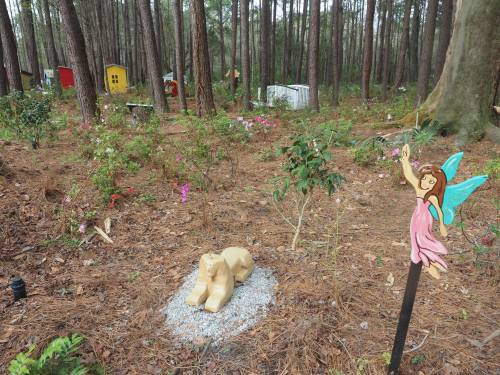 A whimsical forest scene with a fairy statue, a lion figure, and colorful structures among trees and flowers.