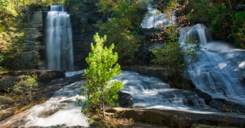 A serene waterfall cascading over rocks, surrounded by lush greenery and sunlight filtering through the trees.