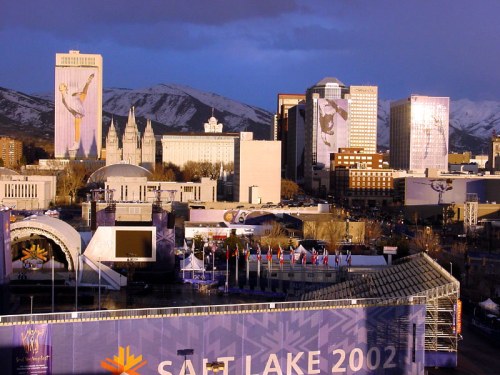 A panoramic view of Salt Lake City with mountains, buildings, and banners for the 2002 Winter Olympics.