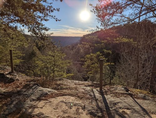A scenic view of a valley with trees and a bright sun shining in the sky, casting light on rocky terrain.