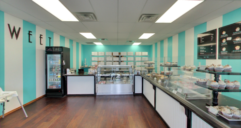 Brightly colored bakery interior with striped walls, display cases of cupcakes, and a drink fridge.