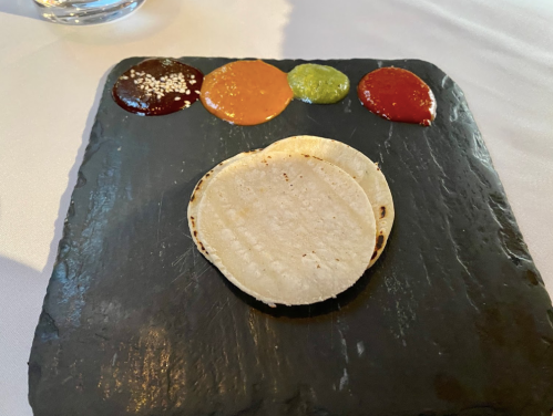 A slate plate with three colorful sauces and two empty tortillas arranged in the center.