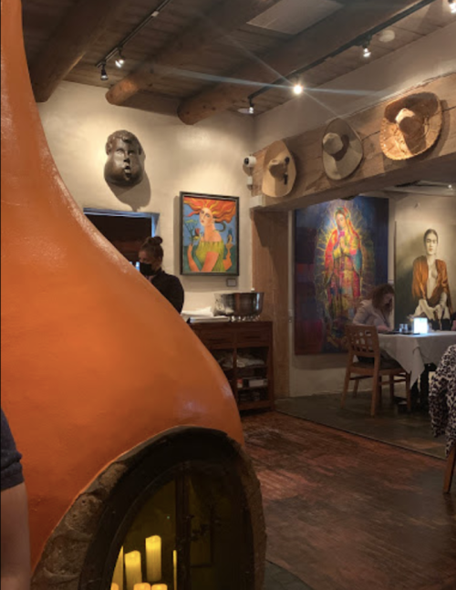 Cozy restaurant interior featuring an orange fireplace, colorful artwork, and decorative masks on the walls.
