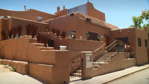 A southwestern-style adobe building with a staircase, decorative railings, and desert landscaping.