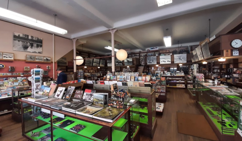 A cozy bookstore filled with shelves of books, magazines, and vintage items, featuring warm lighting and wooden decor.
