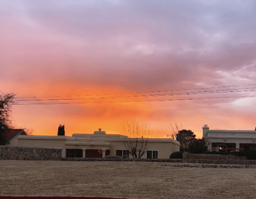 A serene sunset with vibrant orange and pink hues over a suburban landscape and houses.