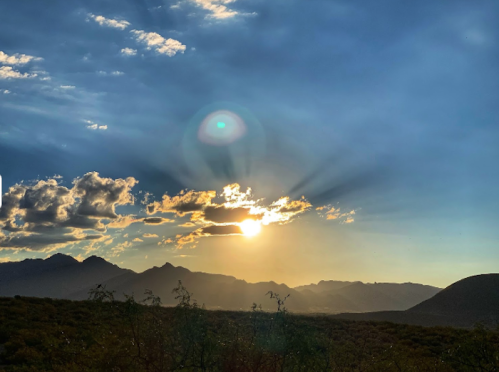 A stunning sunset over mountains, with rays of light breaking through clouds against a blue sky.