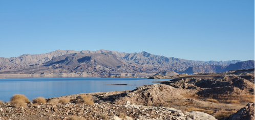 A serene landscape featuring a calm lake surrounded by rocky mountains under a clear blue sky.