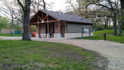 A small, modern building with a sloped roof, surrounded by grass and trees, located in a park setting.