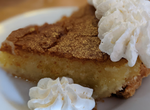 A slice of golden dessert topped with whipped cream, served on a white plate.