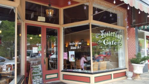 Exterior of Yesterday Cafe with large windows, a sign, and festive decorations. Chairs visible inside.