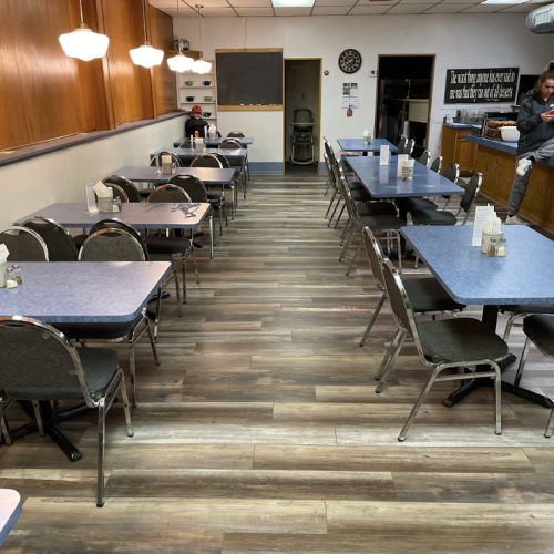 A spacious diner with blue tables and chairs, featuring a long aisle and a person sitting on a counter.
