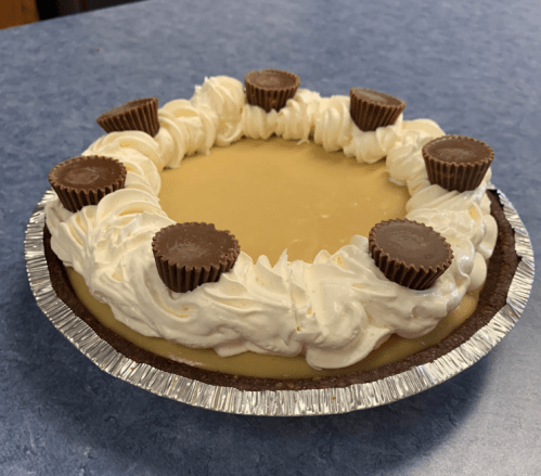 A creamy pie topped with whipped cream and mini chocolate peanut butter cups, in a silver pie crust.
