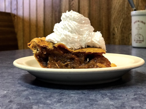 A slice of pie topped with whipped cream on a white plate, set on a blue table.