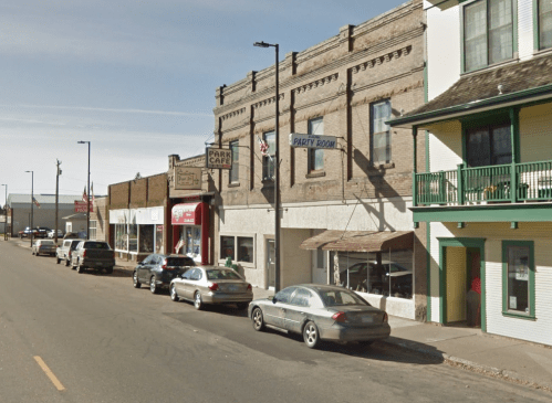 A street view of a small town with parked cars and buildings, including a café and a party room sign.