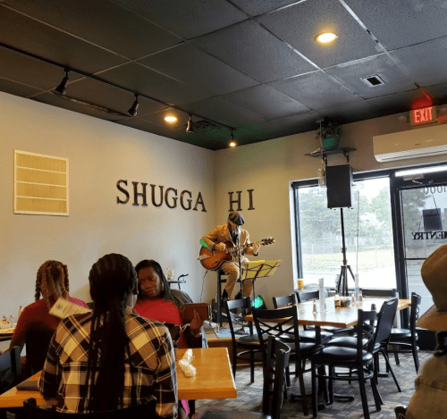A musician performs on stage in a cozy restaurant, with patrons enjoying their meals and the ambiance.