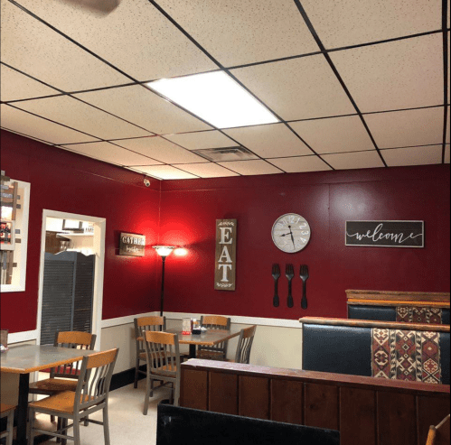 Cozy restaurant interior with red walls, wooden tables, and decorative signs saying "EAT" and "welcome."