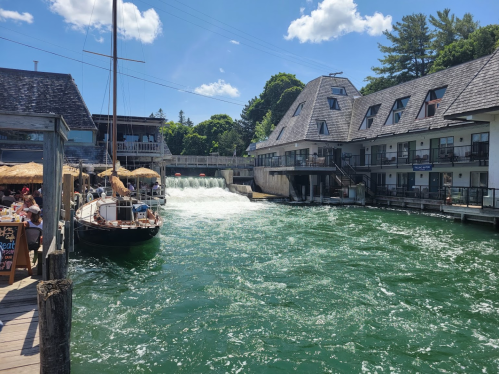 A scenic view of a marina with a boat, waterfall, and buildings under a clear blue sky.