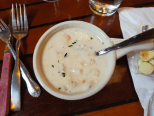 A bowl of creamy seafood chowder garnished with herbs, served on a wooden table with utensils nearby.