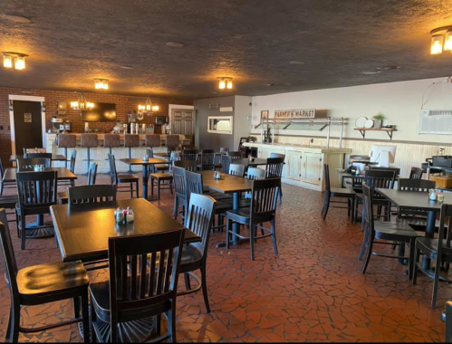 Interior of a restaurant featuring wooden tables and chairs, a counter, and a cozy, rustic atmosphere.
