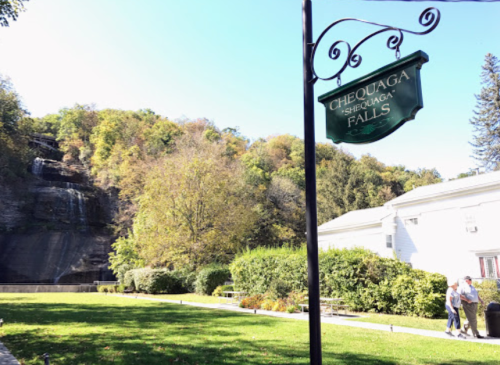 Sign for Chequaga Falls with a waterfall and lush greenery in the background on a sunny day.