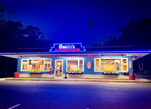A brightly lit restaurant at night, featuring blue exterior and colorful signage, surrounded by trees.