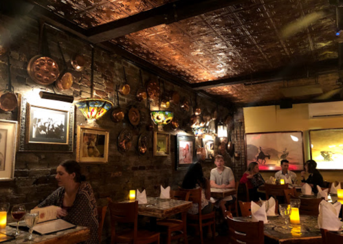 Cozy restaurant interior with brick walls, decorative plates, and patrons dining at wooden tables under warm lighting.