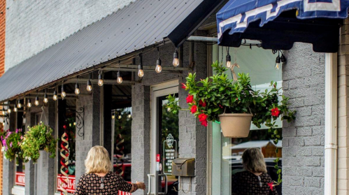 A woman approaches a storefront adorned with hanging plants and string lights, creating a welcoming atmosphere.