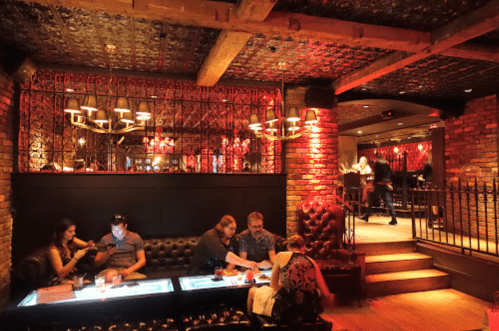 A dimly lit bar with brick walls, plush seating, and patrons enjoying drinks and conversation.