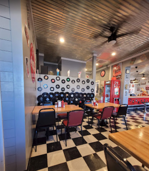 Interior of a retro-style diner with checkered floors, wooden tables, and a wall decorated with vinyl records.