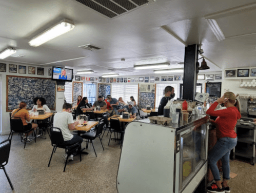 A busy diner with patrons eating at tables and a staff member serving at the counter, decorated with photos on the walls.
