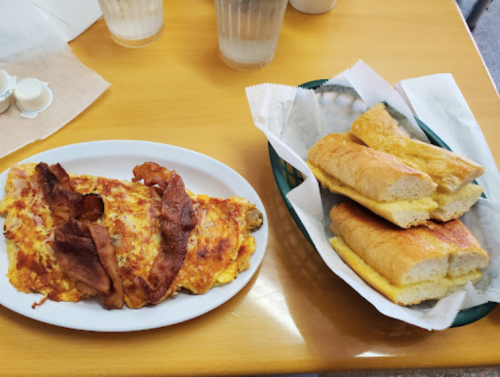 A plate of cheesy omelette topped with bacon, alongside a basket of toasted bread rolls.