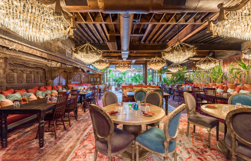 Elegant restaurant interior with ornate chandeliers, wooden beams, and colorful seating, creating a warm, inviting atmosphere.