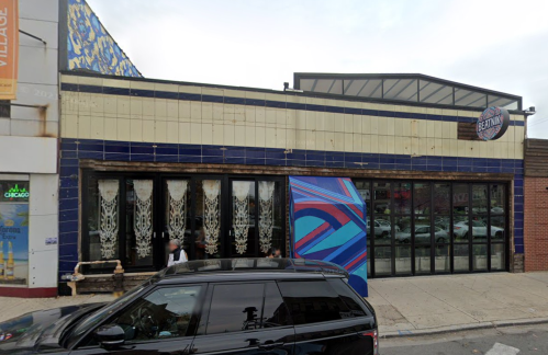 A storefront with a tiled facade, large windows, and colorful mural, set in an urban environment.