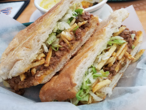 A close-up of a sandwich filled with ground meat, lettuce, and fries, served in a toasted bread.
