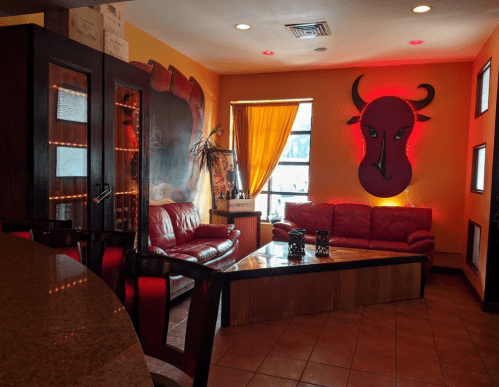 Cozy lounge area with red leather sofas, a wooden coffee table, and a bull mural, illuminated by warm lighting.
