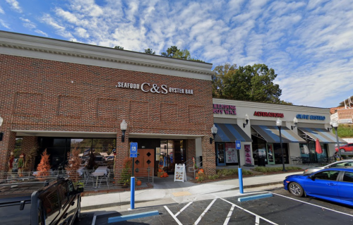 Exterior view of a seafood restaurant and adjacent businesses, with a blue sky and parked cars in front.