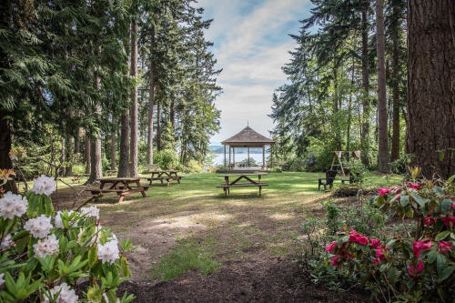 A serene outdoor scene with picnic tables, a gazebo, and lush greenery leading to a lake view.
