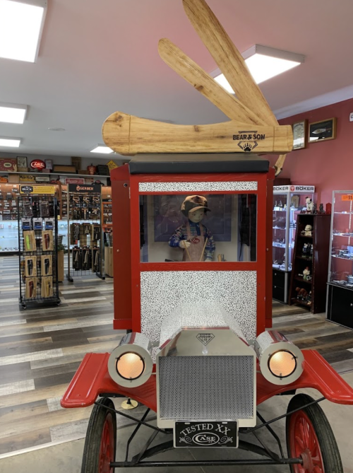 A vintage car display with a mannequin wearing a hat and large wooden antlers on top, set in a shop interior.