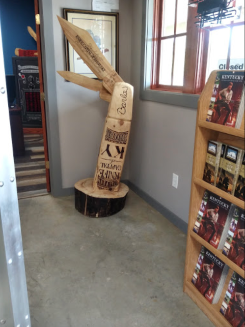 A wooden sculpture with engraved designs, displayed in a room with brochures and a framed picture on the wall.