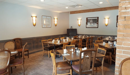 Cozy restaurant interior with wooden tables, chairs, and soft lighting, set for dining with condiments on tables.