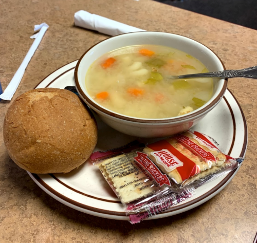 A bowl of soup with carrots and celery, served with a roll and crackers on a plate.