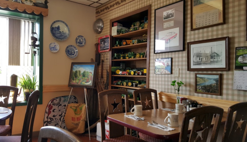Cozy restaurant interior with wooden tables, vintage decor, and shelves displaying collectibles and artwork.