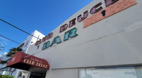 Sign for Club Deuce Bar against a clear blue sky, featuring colorful letters and a decorative design.